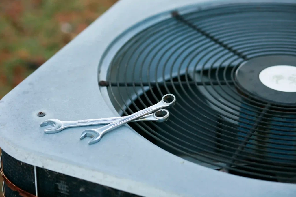 AC Replacement In Ellenwood, GA 1 Two wrenches resting on the fan grille of an outdoor air conditioning unit, symbolizing HVAC repair and maintenance tools.