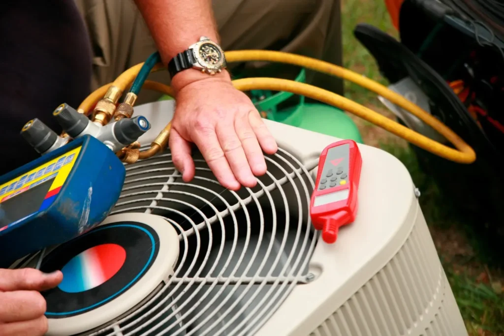 AC Tune-Up in Stonecrest, GA 1 A close-up shows a person's hands working with gauges and a thermometer on top of an outdoor air conditioning unit. Yellow and green hoses are also visible.