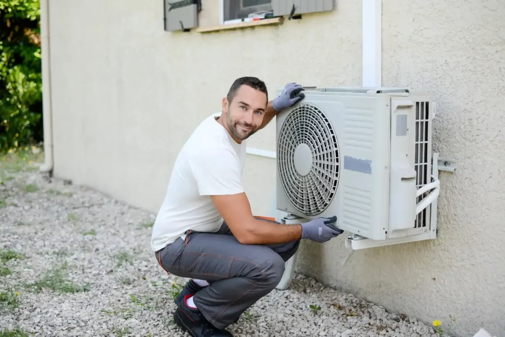 HVAC Service in Stonecrest, GA 1 A man dressed in white shirt is trying to repair a mini split and looking at the camera smiling
