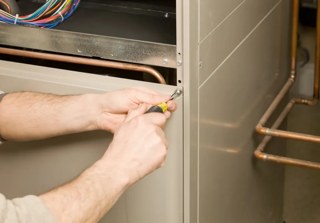 Furnace Installation In Ellenwood, GA 1 Technician using a screwdriver to adjust the side panel of an HVAC unit with visible copper pipes and electrical wiring during maintenance