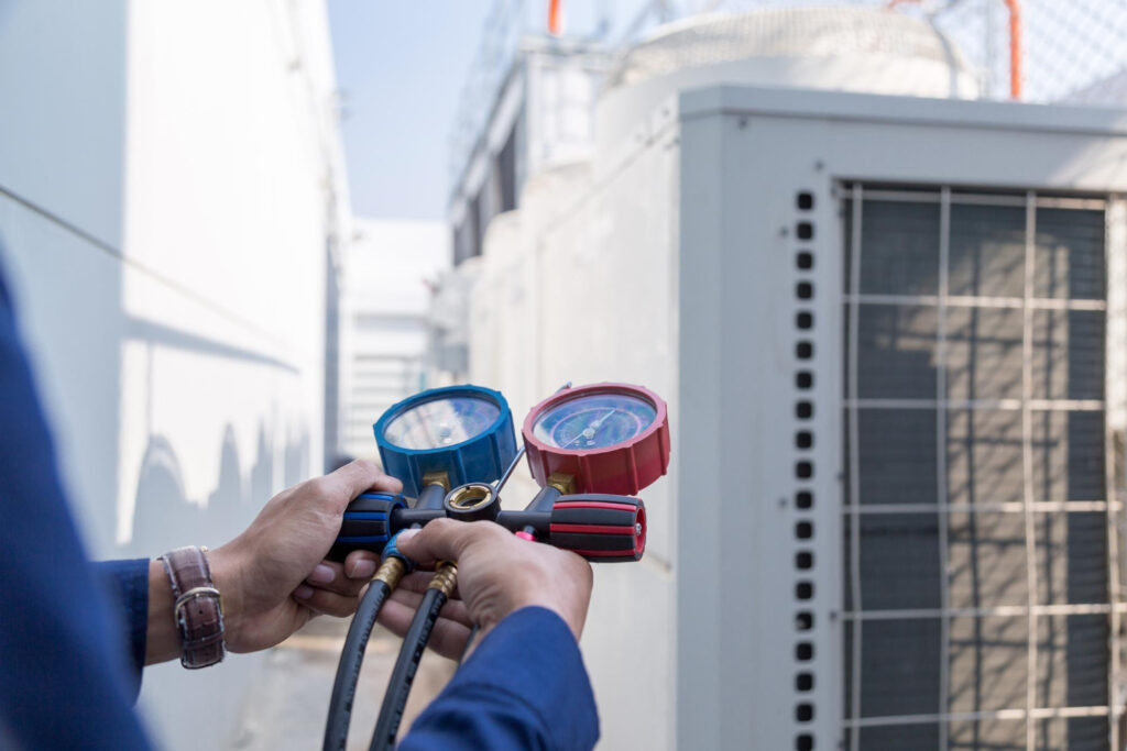 HVAC technician holding pressure gauges in front of an outdoor cooling unit, emphasizing professional maintenance and check-ups for air conditioning systems.